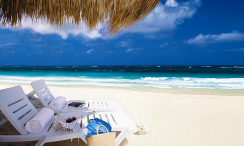 two empty beach chairs under an umbrella on the beach looking out at the ocean