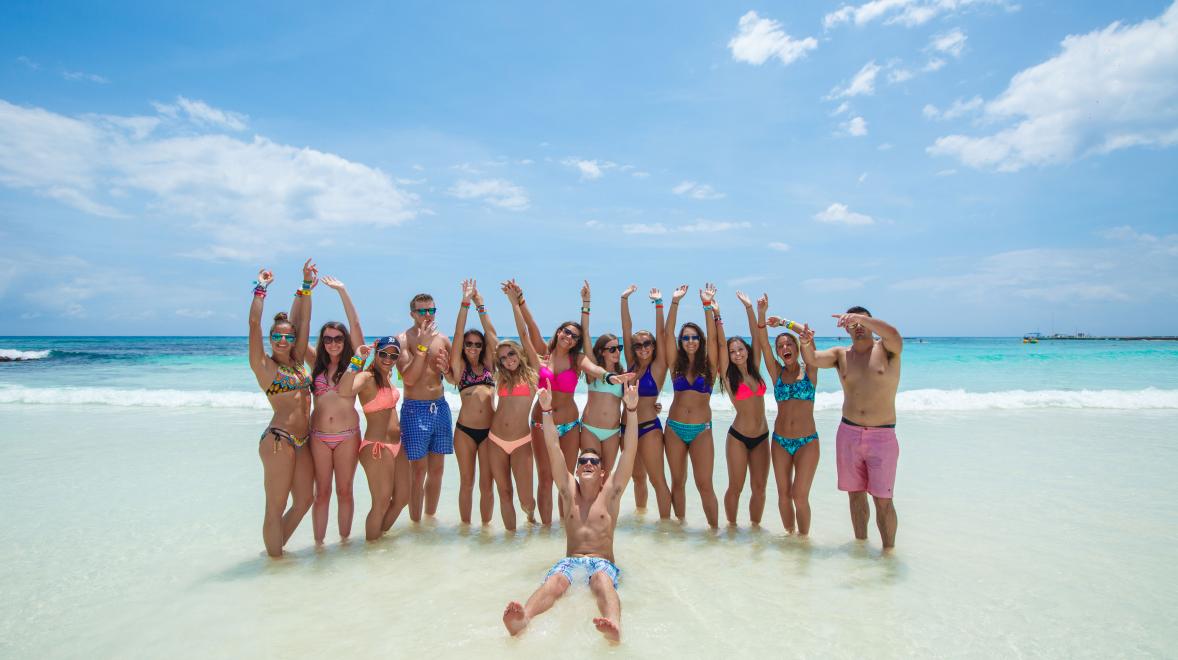 High schoolers throwing up their hands on a group photo shoot on the beach. 